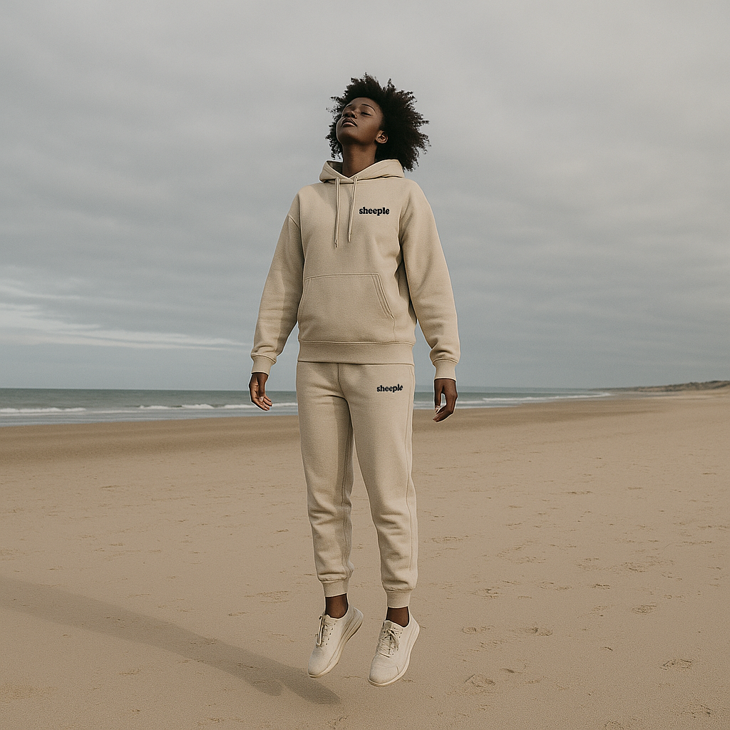 Person wearing a beige tracksuit on a beach with a cloudy sky