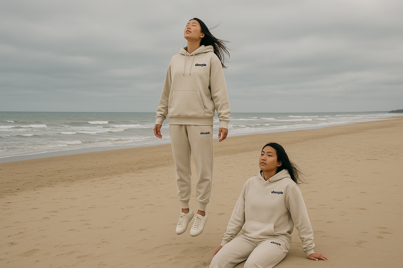 Two people in matching beige sweatsuits on a beach with ocean waves in the background.