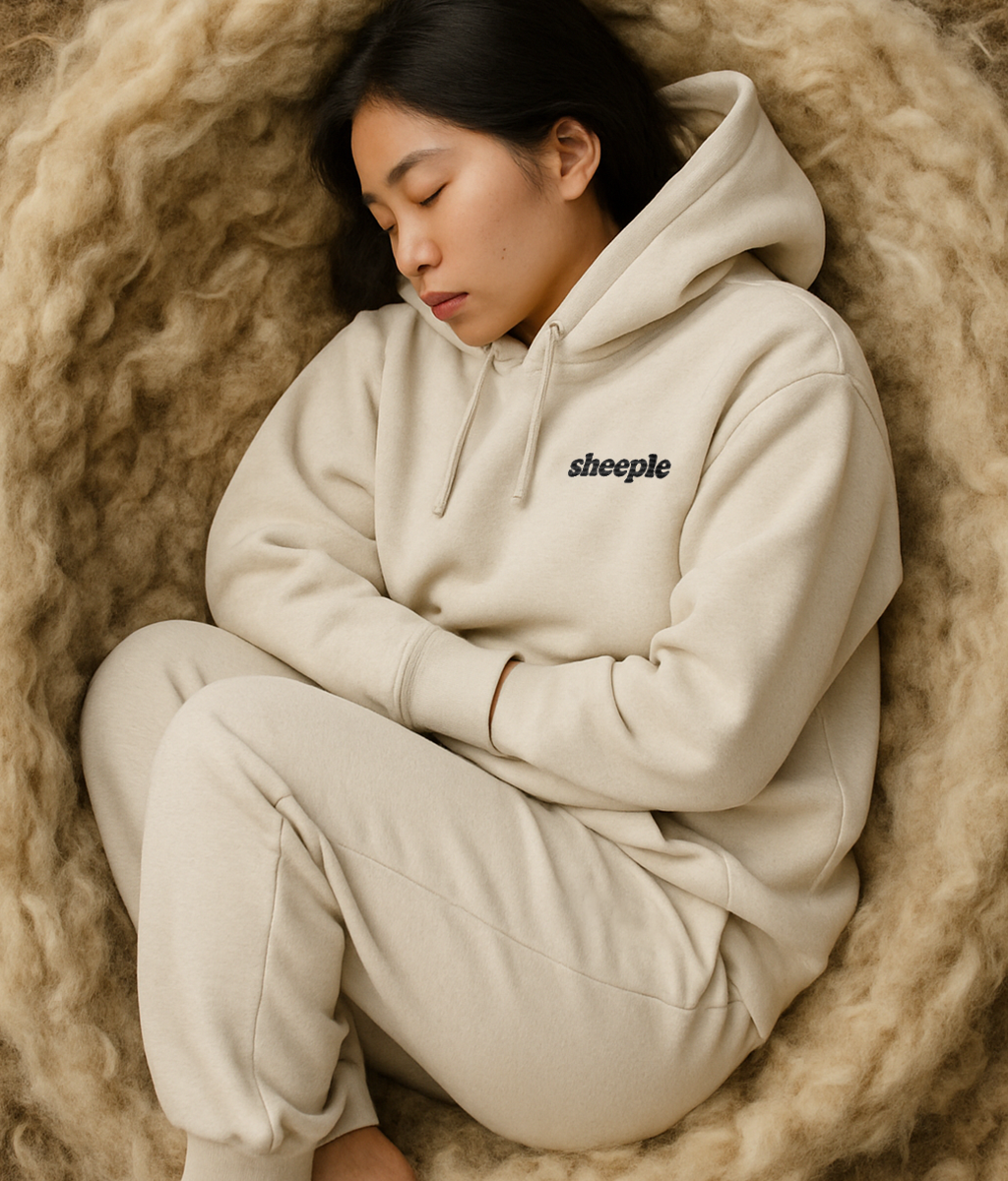 Person wearing a beige 'sheeple' hoodie sitting inside a circular arrangement of wool.